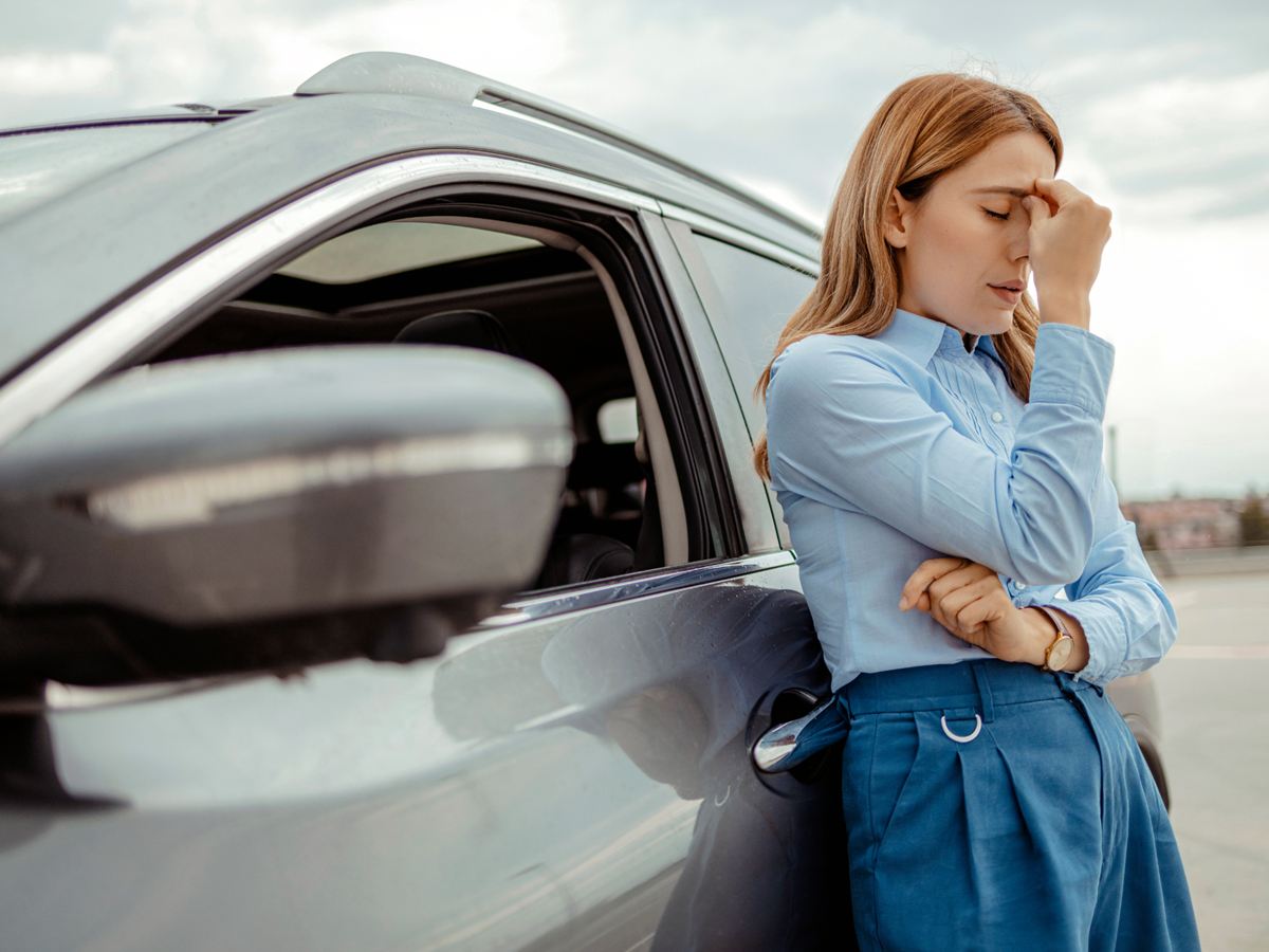 Nachdenkliche Frau lehnt mit der Hand an der Stirn an ihrem Auto
